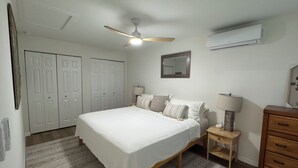 Een slaapkamer met een bed, nachtkastjes, een plafondventilator, een spiegel en een kledingkast.