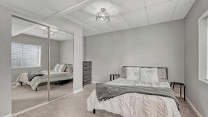 A bedroom with a large mirror, a bed with a gray comforter, a wooden dresser, and a ceiling light fixture. - Delightful 1-bedroom apartment in Castle Rock - close to the Hospital (Castle Rock)
