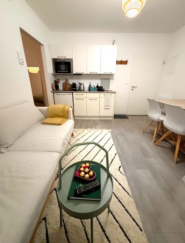 Un espace de vie compact comprenant un canapé, une petite table à manger, un coin cuisine et une chaise.