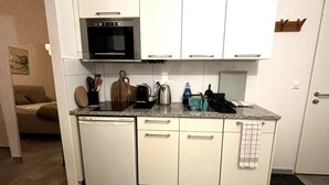 Una cocina compacta con armarios blancos, horno integrado, cafetera y lavavajillas.