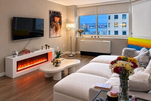 Ein modernes Wohnzimmer mit Kamin, Flachbildfernseher, einer Couch und Blick auf eine Stadtlandschaft durch große Fenster.
