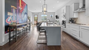 Una cocina moderna con una isla grande, taburetes de bar, una campana extractora de acero inoxidable y un ventanal que proporciona luz natural.
