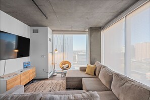 A modern living room with a large flat-screen TV, a sofa, a wooden cabinet, and a chair. - Premium Stay 2mins to PHX Convention Ctr (Phoenix)