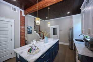 A modern kitchen with a marble island, dark blue cabinets, and a brick accent wall. - Coastal Cove-Near Beach with a Game room (Galveston)