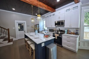 A modern kitchen with white cabinets, a central island, stainless steel appliances, and pendant lighting. - Coastal Cove-Near Beach with a Game room (Galveston)