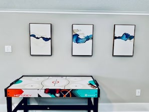 A hockey table with 'Hockey' branding, three abstract paintings on the wall, and a light gray wall. - Coastal Cove-Near Beach with a Game room (Galveston)