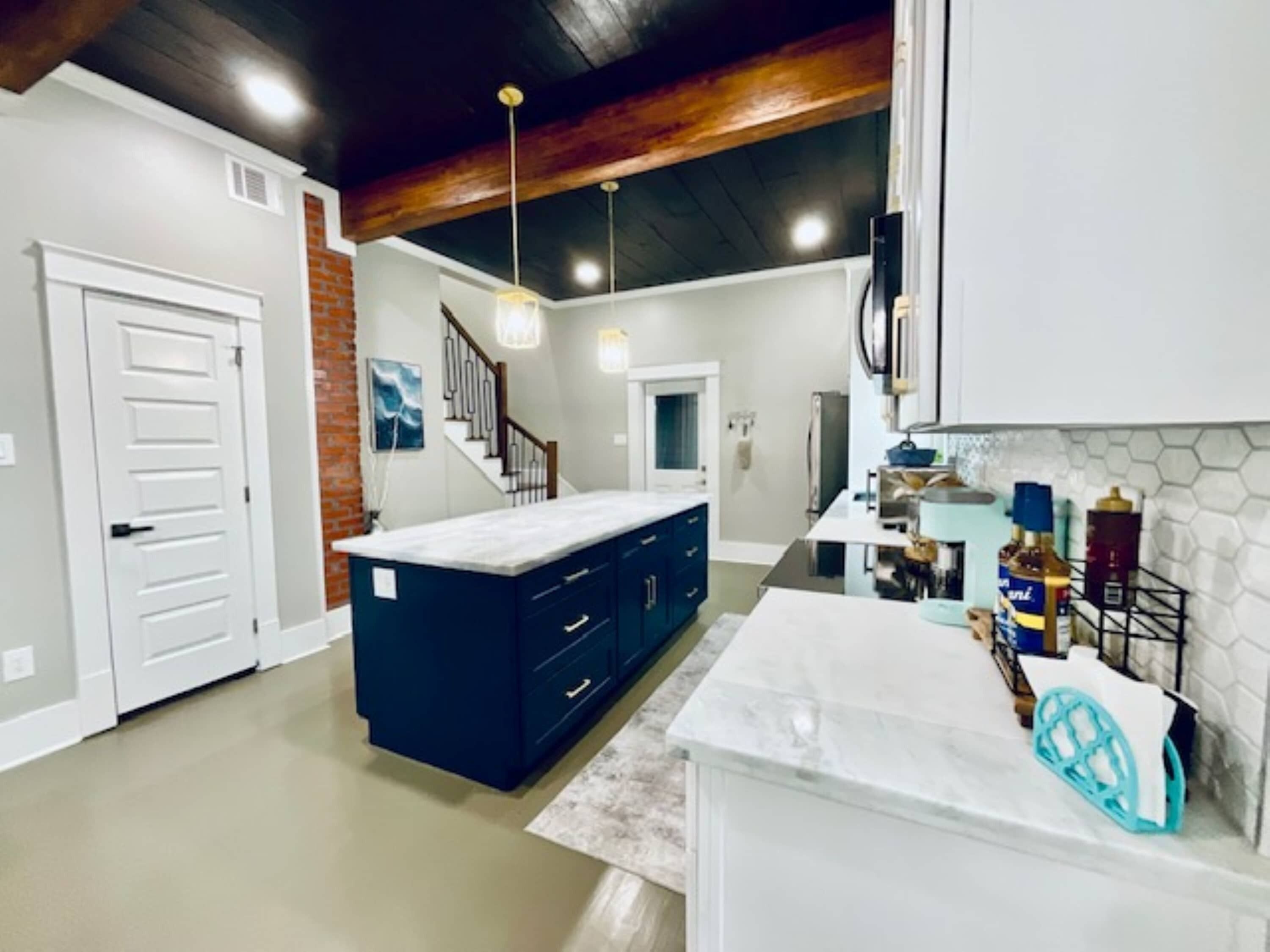 A modern kitchen with dark blue cabinets, a white countertop, and a brick accent wall.