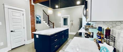 A modern kitchen with dark blue cabinets, a white countertop, and a brick accent wall.