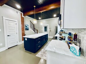 A modern kitchen with dark blue cabinets, a white countertop, and a brick accent wall. - Coastal Cove-Near Beach with a Game room (Galveston)