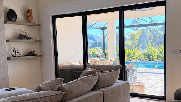 A modern living room with a sectional sofa, a wooden dining table, and a view of an outdoor pool area.