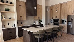 A modern kitchen with wooden cabinets, a central island with bar stools, built-in appliances, and pendant lighting.