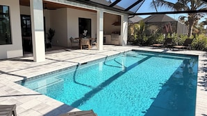 A swimming pool with a covered patio area, lounge chairs, and a view of the house.