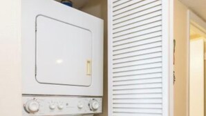A compact laundry room with a washer and dryer, a door with horizontal louvered panels, and a visible light switch. - Our 3 bedroom unit is expansive, and perfect for large parties going on vacation (North Myrtle Beach)
