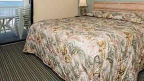 A hotel room with a bed, a ceiling fan, a nightstand, a lamp, a framed picture on the wall, and a view of the ocean through a sliding door. - Our 3 bedroom unit is expansive, and perfect for large parties going on vacation (North Myrtle Beach)
