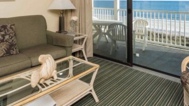 A hotel room with a sofa, a small table, a lamp, a ceiling fan, and a view of the ocean through a sliding glass door. - Our 3 bedroom unit is expansive, and perfect for large parties going on vacation (North Myrtle Beach)