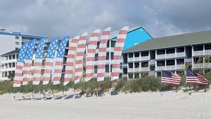 A beach with flags, a building with balconies, and a clear sky. - Our 3 bedroom unit is expansive, and perfect for large parties going on vacation (North Myrtle Beach)