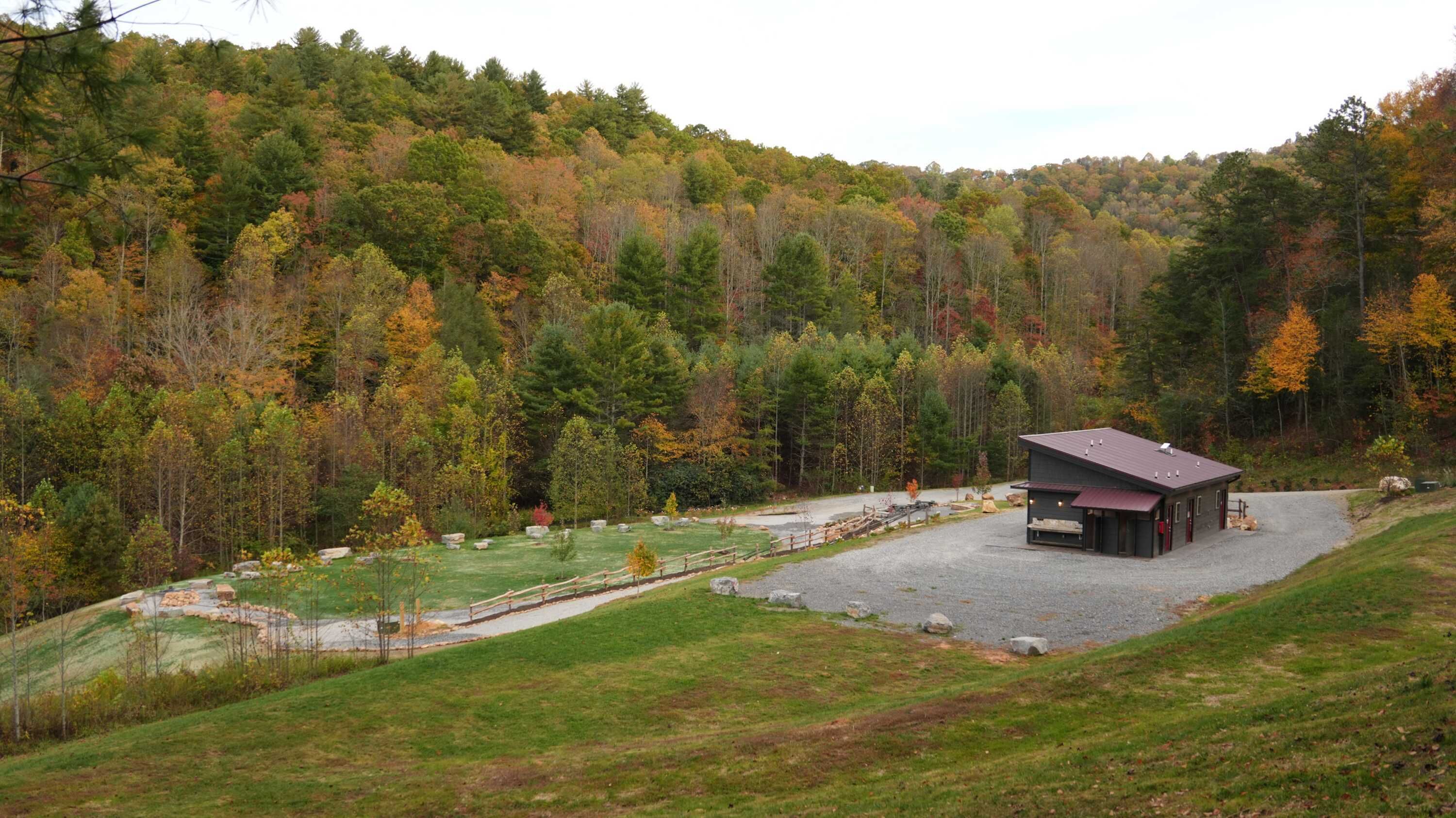 A lodge with a gravel driveway, a fenced yard, and a forested backdrop.