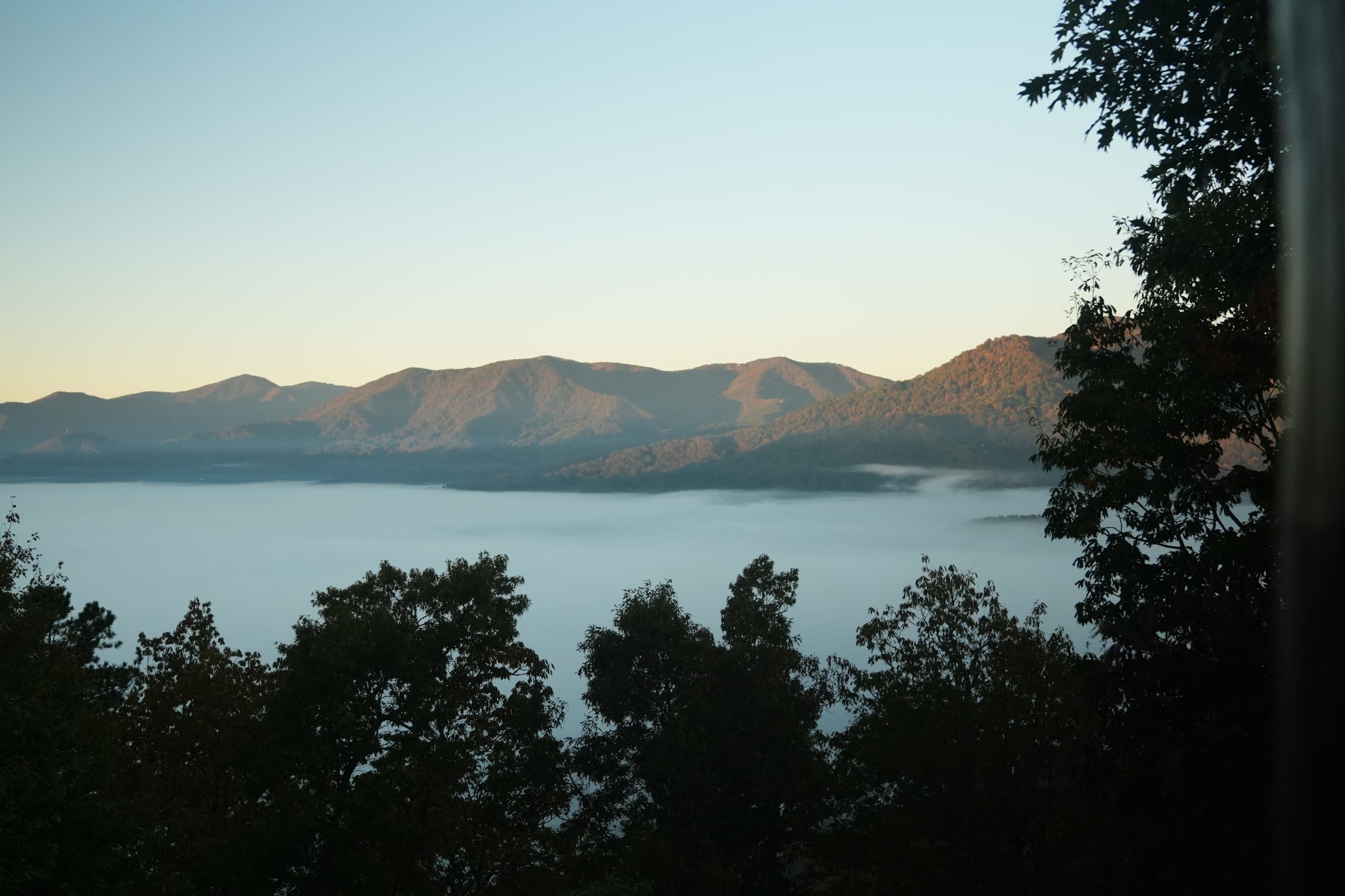 Una cordillera con un lago en primer plano y árboles al frente.