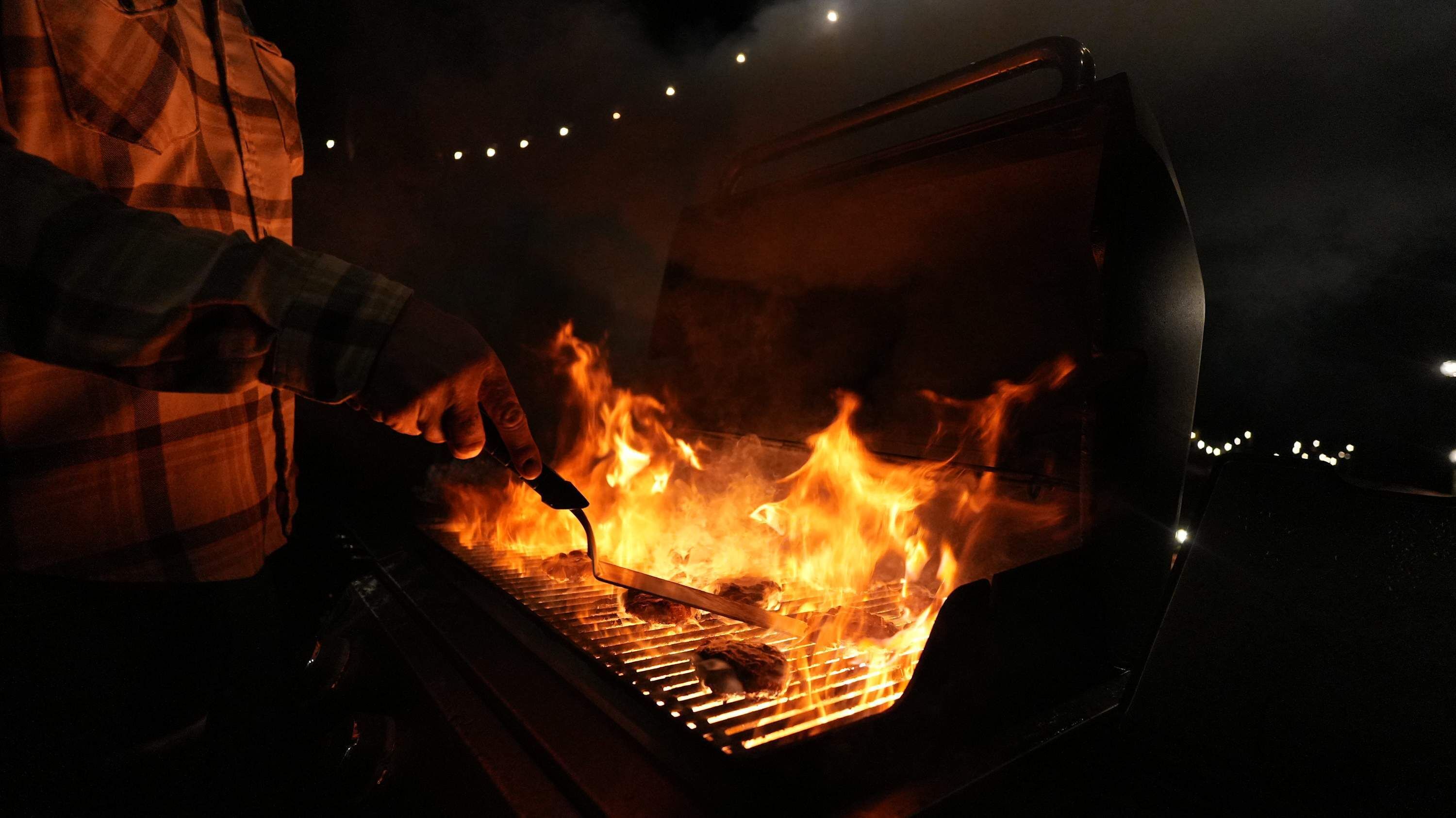 Une personne qui fait griller de la viande sur un barbecue portable, la nuit.