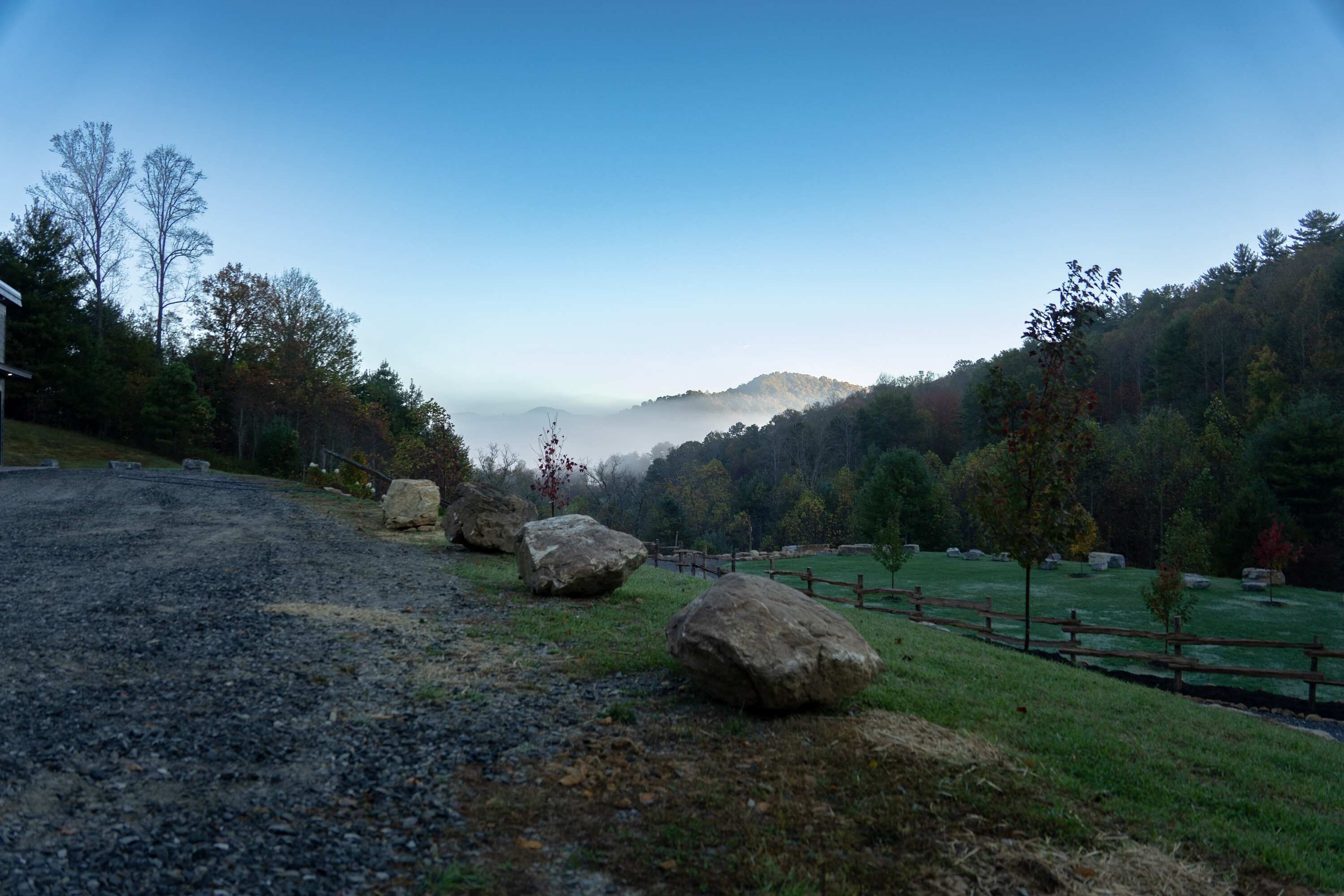 A gravel path leading to a grassy area with large rocks and a wooden fence.