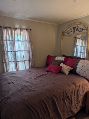 A bedroom with a large bed, a mirror, and sheer curtains. - Cozy 2-bedroom house in peaceful Bloomington Springs with AC (Bloomington Springs)