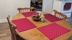 Un comedor con una mesa redonda de madera, individuales rojos y un centro de mesa con frutero.