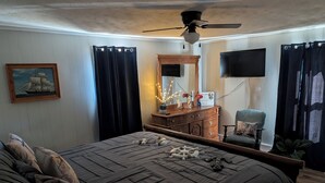 Un dormitorio con cama, cómoda, silla, espejo, cuadro y ventilador de techo.