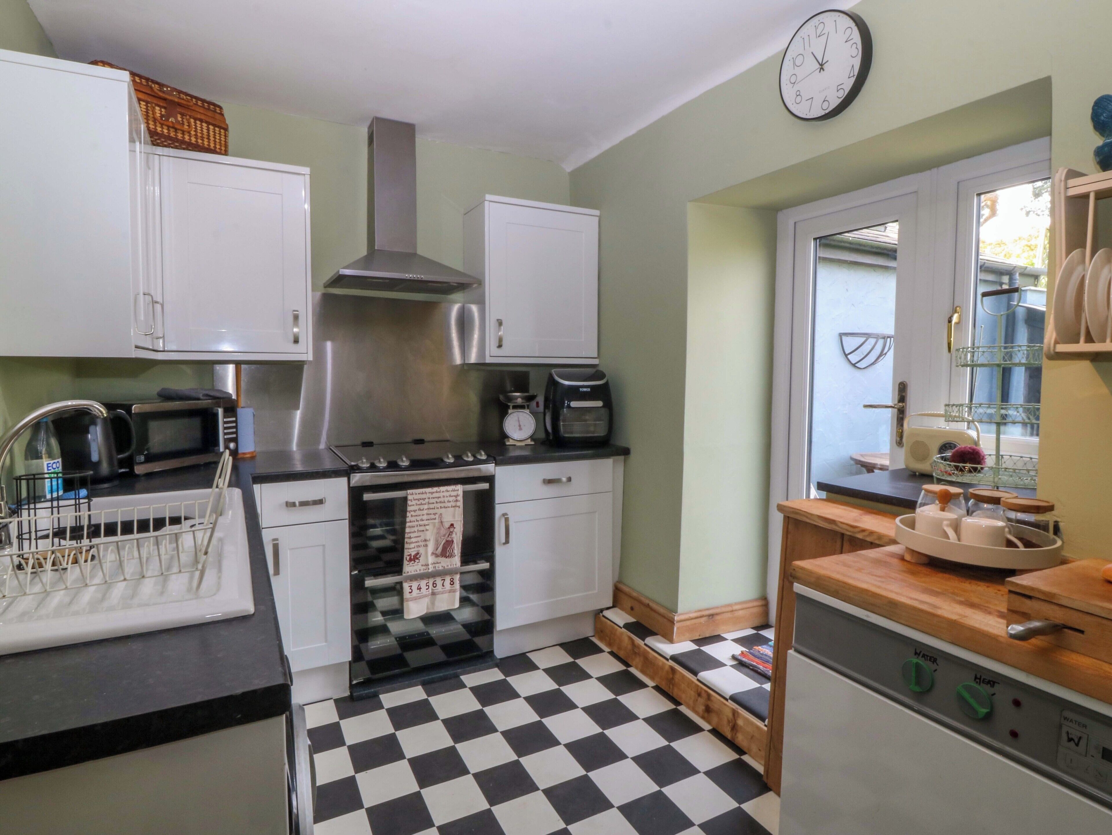 A kitchen with white cabinets, a stainless steel range hood, a microwave, a kettle, and a checkered floor.