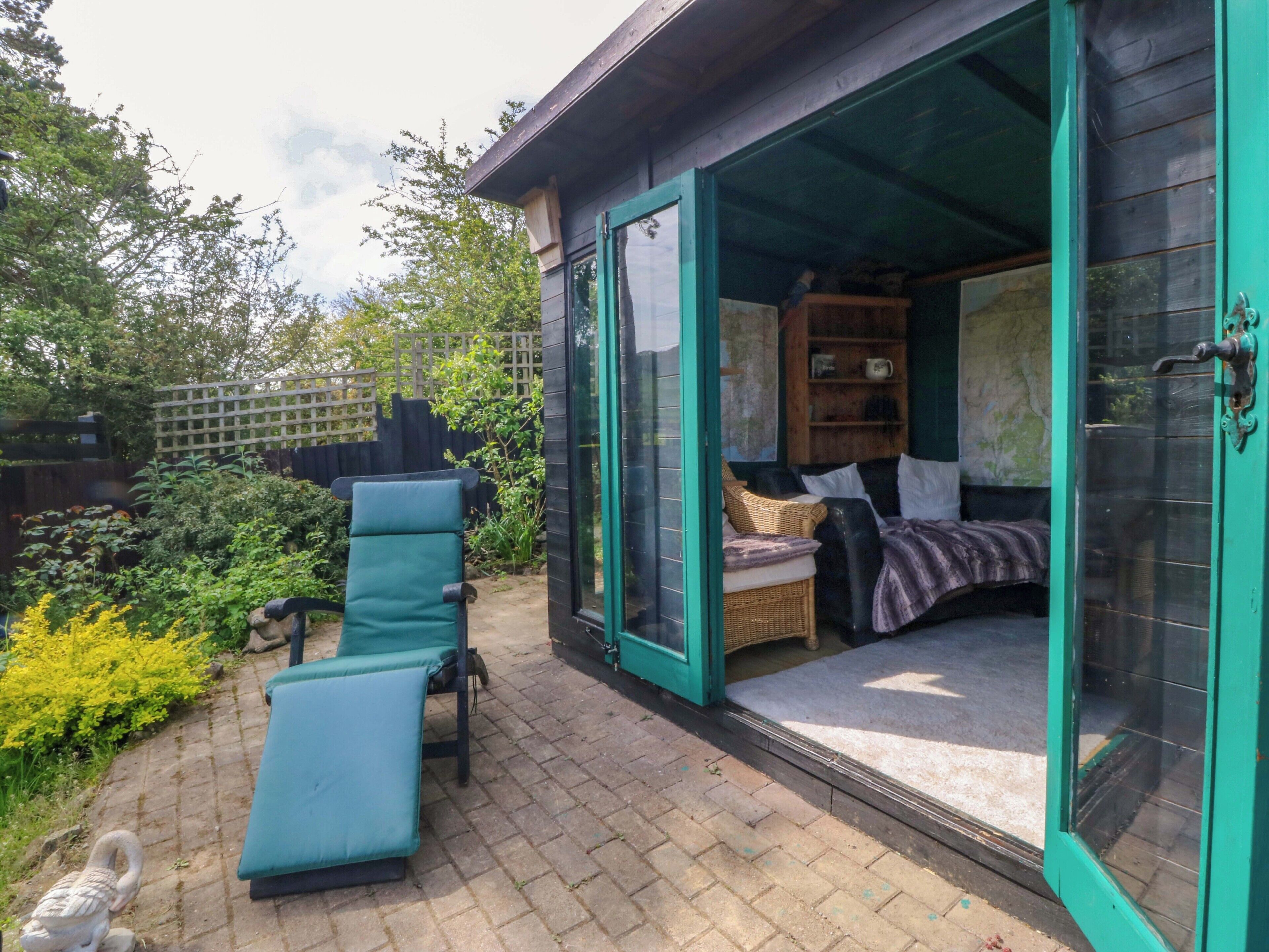 A cozy outdoor seating area with a lounge chair and a small table, a wooden bench, and a wicker chair.
