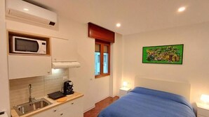 A compact room with a bed, a kitchenette with a microwave, a sink, and a window. - PRINCE APARTMENT STUDIO (Napoli)
