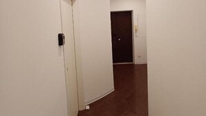A hallway with white walls and a brown tiled floor, leading to a dark door at the end. - PRINCE APARTMENT STUDIO (Napoli)