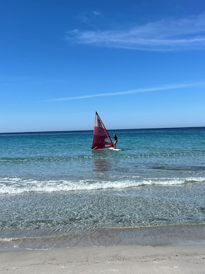 Ein Strand mit klarem Wasser und einer Person, die Windsurfen geht.