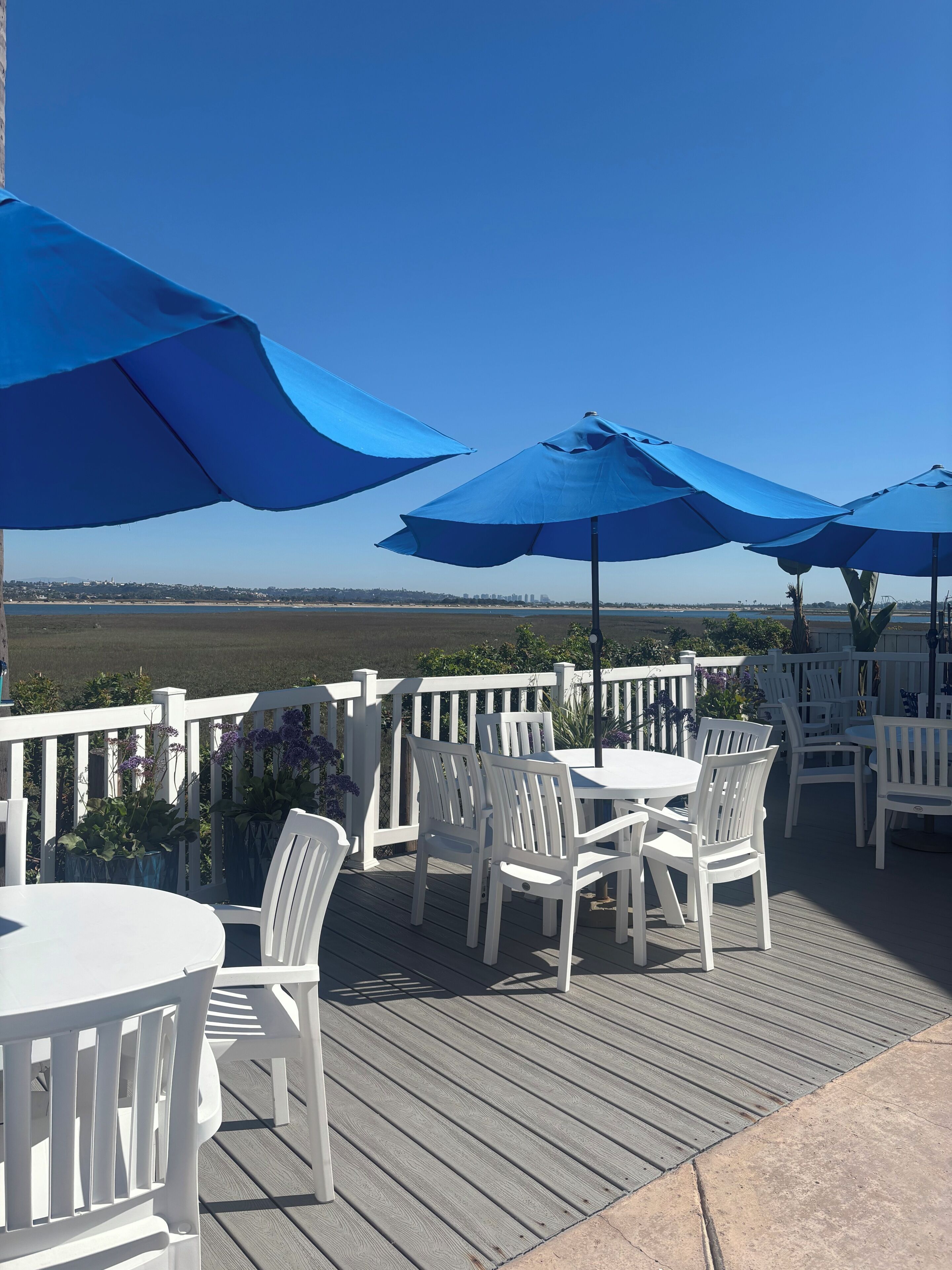 A deck with white chairs and blue umbrellas, overlooking a body of water.