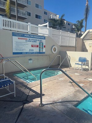 Ein Poolbereich mit einem Schild, das Schwimm- und Spa-Bestimmungen, einschließlich Rettungsschwimmerpflicht und Personenbegrenzung, detailliert beschreibt.