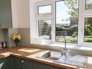 A kitchen with a stainless steel sink, a window with a view of a garden, and a vase with flowers on the counter. - Seashells at Runswick Lodge (Saltburn-by-the-Sea)