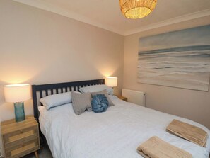 A neatly made bed with patterned pillows, a bedside lamp, a nightstand, and a painting of a beach scene. - Seashells at Runswick Lodge (Saltburn-by-the-Sea)