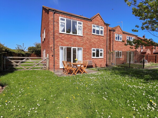 A two-story brick house with a patio, a wooden gate, and a lawn with flowers. - Seashells at Runswick Lodge (Saltburn-by-the-Sea)