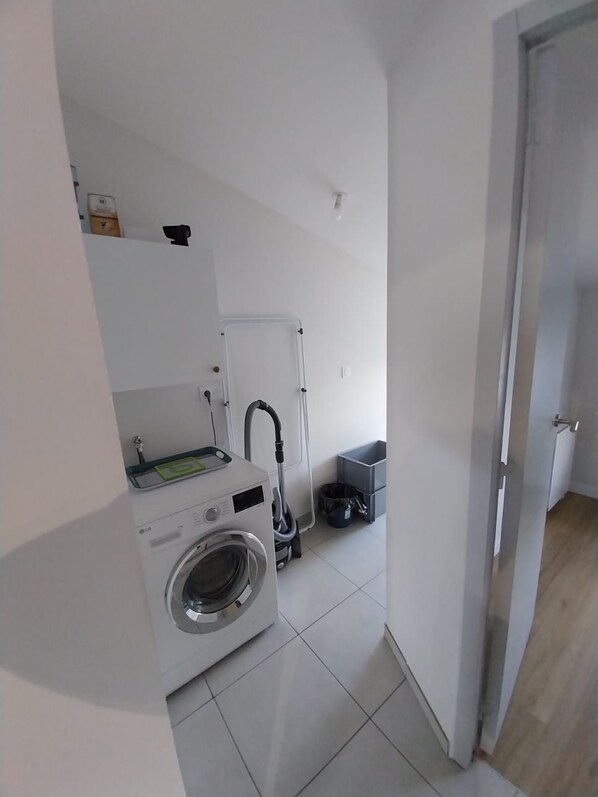A compact laundry area with a washing machine, a drying rack, and a vacuum cleaner. - La Caillère Vacation Rental for 4 People (Moncoutant-sur-Sèvre)