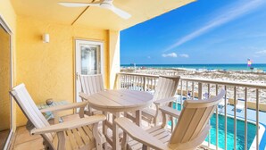 Een balkon met een tafel en stoelen, een plafondventilator en uitzicht op het strand en de oceaan.