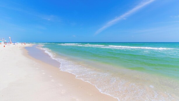 Een strand met helderblauw water, een zandstrand en enkele parasols.