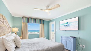 Een slaapkamer met een bed, een plafondventilator, een televisie en uitzicht op het strand.