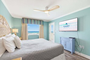 A bedroom with a bed, a ceiling fan, a television, and a view of the beach. - The Big Surf II - Gulf View - Beach, Pool, and Fun (Gulf Shores)