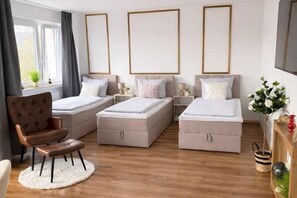A modern bedroom with two beds, a chair, bedside tables, and a window with curtains.