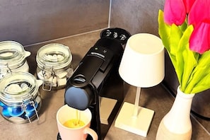A coffee machine, a mug, a vase with flowers, and jars on a kitchen counter.