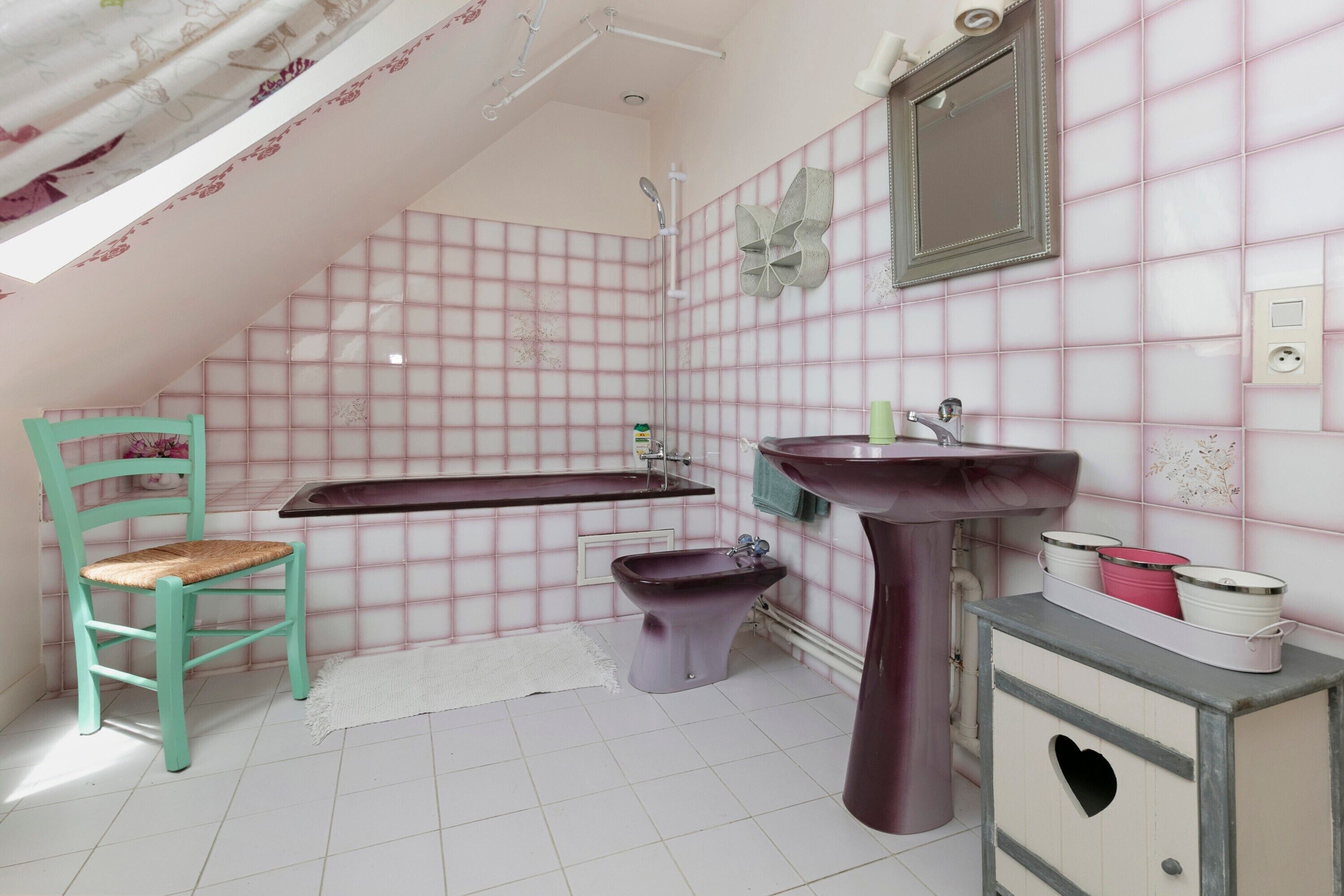 Un baño con bañera, lavamanos pedestal, un bidé, tocador con cajón con forma de corazón y una silla.