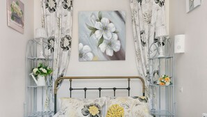 Une chambre à coucher avec un lit, des rideaux à motifs floraux, une lampe fixée au mur et un tableau encadré.