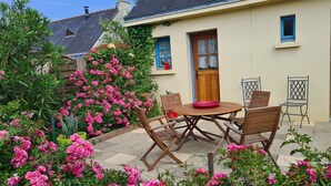 Une maison avec un patio, une table ronde en bois entourée de chaises, une porte en bois et une fenêtre avec des bordures bleues.