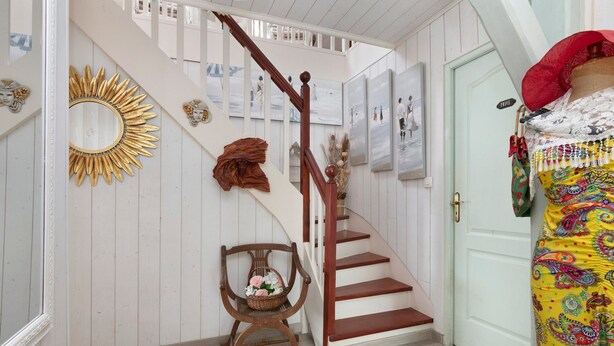 Un escalier avec une rampe en bois, une porte blanche et un mur orné de tableaux encadrés.
