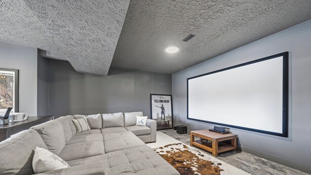 Un salon moderne avec un canapé d’angle, un grand téléviseur à écran plat, un tapis en peau de vache et un projecteur posé sur une table en bois.
