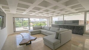 A spacious living area with a large L-shaped sectional sofa, a unique wooden coffee table, and a balcony with a view of greenery and buildings. - Clock Tower PH · PH in the historic center (Cartagena)